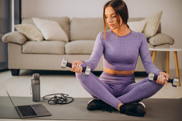 Woman watching tutorials and training from home on mat using skipping rope and dumbbells